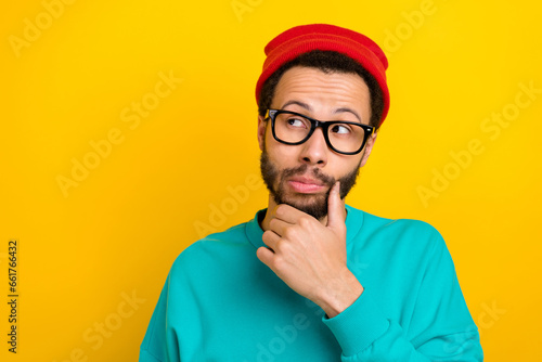 Portrait of ponder suspicious man with beard dressed turquoise pullover arm on chin look empty space isolated on yellow color background