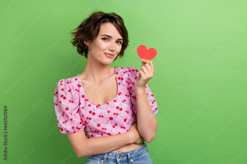 Photo of cute good mood woman with bob hairstyle dressed pink blouse hand holding paper red heart isolated on green color background Photo of cute good mood woman with bob hairstyle dressed pink blouse hand holding paper red heart isolated on green color background