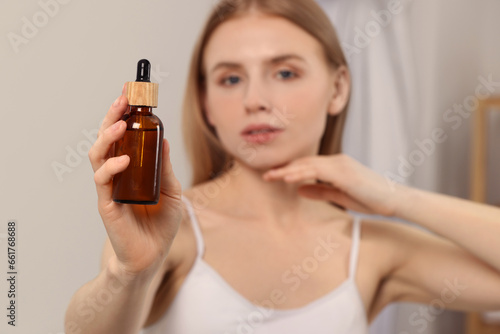 Woman with bottle of essential oil indoors, selective focus. Space for text