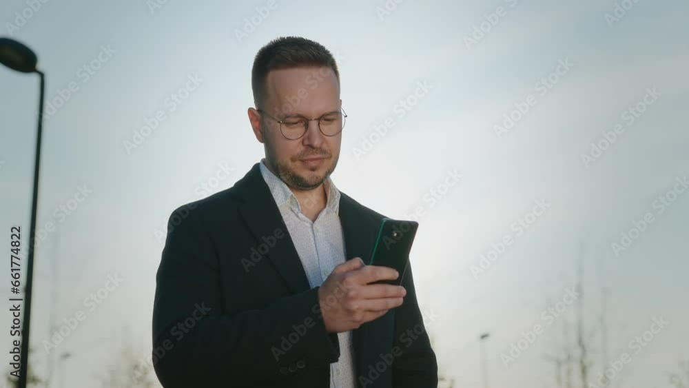 Elegant urban man in a coat and glasses in the park. A businessman uses a smartphone to work in applications and social networks. Elegant urban man in a coat and glasses in the park. A businessman uses a smartphone to work in applications and social networks.