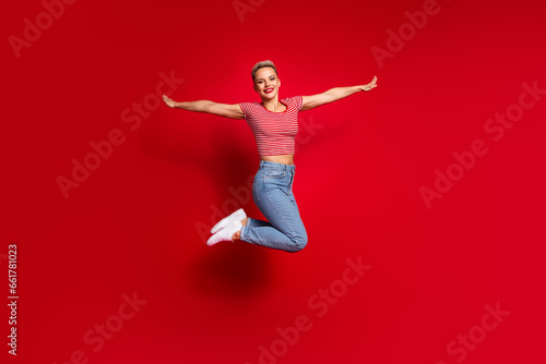 Full length photo of glad optimistic girl wear trendy striped clothes open hands rejoice summer vacation isolated on red color background