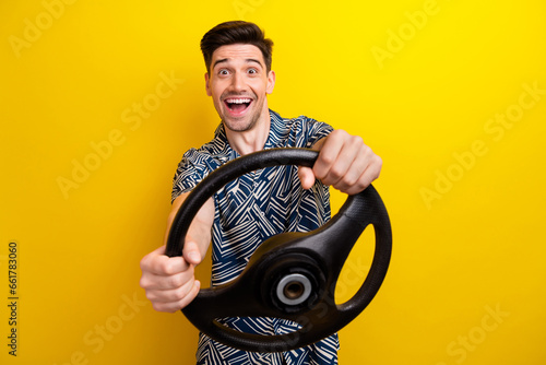 Portrait of astonished positive man arms hold steering wheel open mouth isolated on yellow color background