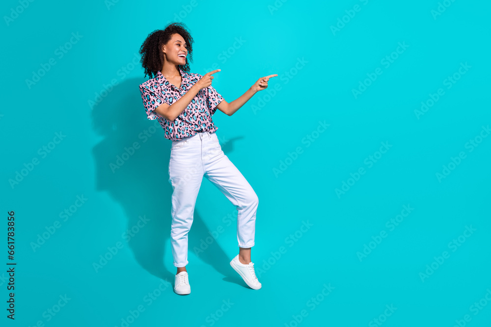 Full length photo of cheerful adorable girl wear stylish clothes two hands presenting empty space banner isolated on cyan color background Full length photo of cheerful adorable girl wear stylish clothes two hands presenting empty space banner isolated on cyan color background