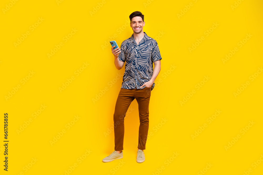 Full size photo of pleasant smart guy wear stylish shirt trousers hold smartphone read notification isolated on yellow color background Full size photo of pleasant smart guy wear stylish shirt trousers hold smartphone read notification isolated on yellow color background