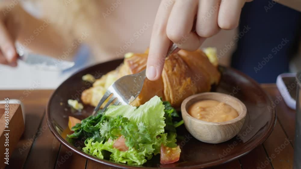 Close-up, Woman with knife and fork, hands cut croissant with mozzarella, salad leaves. Delicious nutritious aromatic dish with unusual taste. Croissant on plate. Slow mo Close-up, Woman with knife and fork, hands cut croissant with mozzarella, salad leaves. Delicious nutritious aromatic dish with unusual taste. Croissant on plate. Slow mo