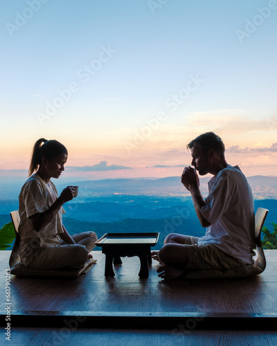 a couple of men and women drinking tea in the mountains of Northern Thailand at the balcony of a wooden hut cabin