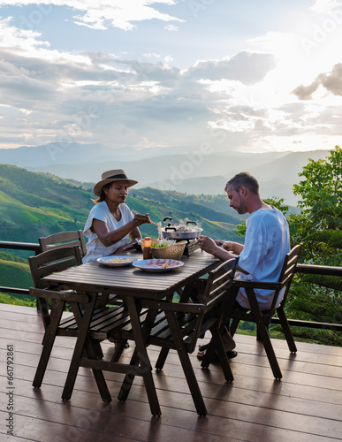 a couple of men and women on vacation in Northern Thailand, staying at a homestay cabin hut in the mountains of Chiang Rai Doi Chang enjoying dinner with a Thai BBQ at sunset in the mountains © Fokke Baarssen