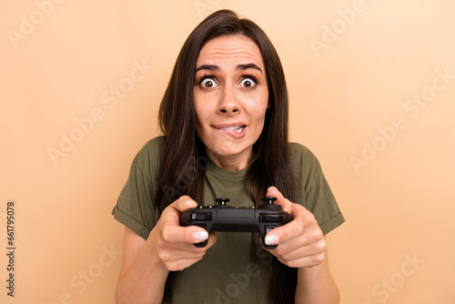 Photo of funky tricky lady wear khaki t-shirt biting lip playing playstation game isolated beige color background