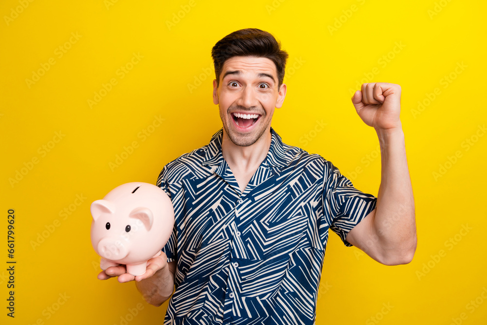 Portrait of delighted positive man hold money pig bank raise fist attainment isolated on yellow color background Portrait of delighted positive man hold money pig bank raise fist attainment isolated on yellow color background