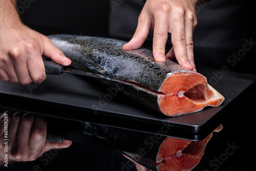 A cook on a black background cuts a whole salmon carcass.