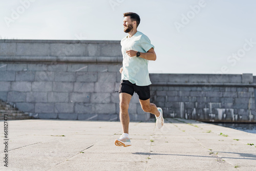 A runner uses a fitness watch on his arm. A sporty young man running alone. Daily training development of the cardiac system. Slim body and active lifestyle.
