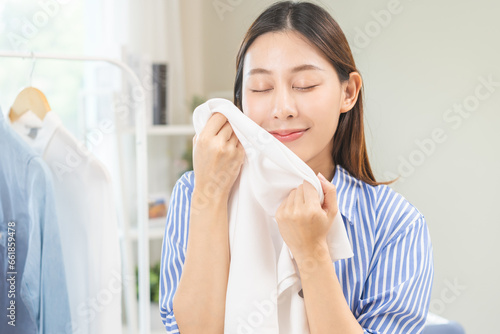 Feel softness, hygiene. Smile asian young woman touching fluffy white shirt smelling fresh clean clothes, pretty girl comfort sniff after washing laundry. Household work at home, chore of maid concept photo