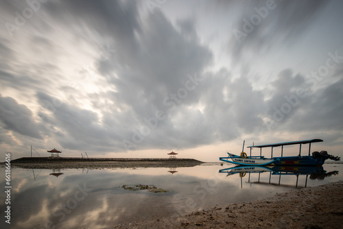 Sunrise at the sandy beach of Sanur. Temple in the water. Traditional fishing boat  Jukung on the beach. Hindu faith in Sanur on Bali. Dream island and dream destination