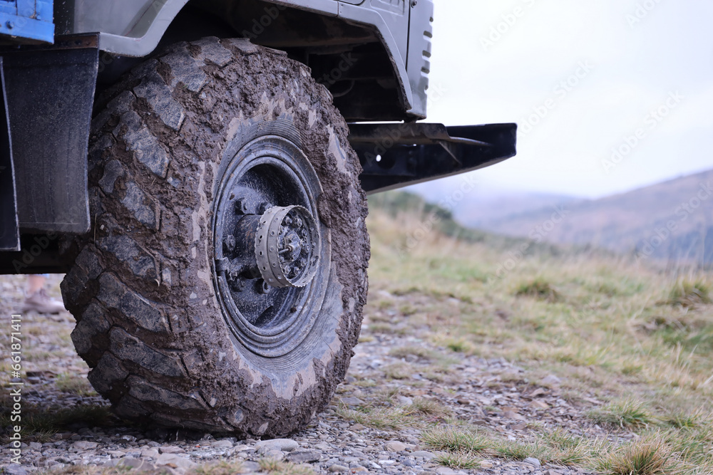 Wheel closeup in a countryside landscape with a mud road. Off-road 4x4 suv automobile with ditry body after drive in muddy road