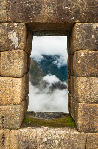 View from an ancient window in Machu Picchu. There is mountains and clouds in the background
