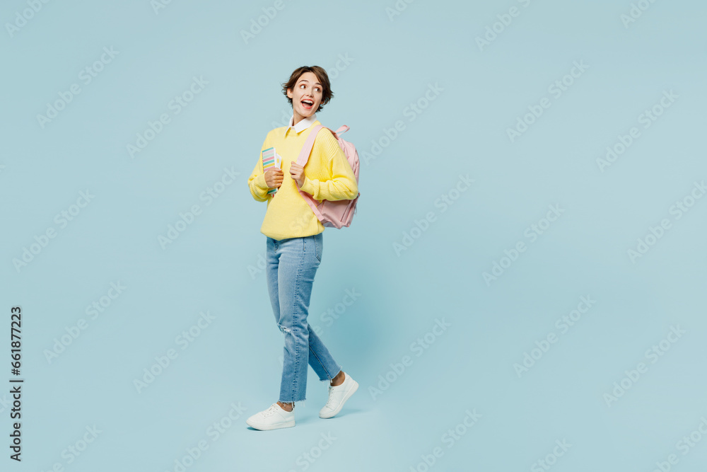 Full body side view young woman student wear casual clothes sweater backpack bag hold books look aside on area walk go stroll isolated on plain blue background. High school university college concept. Full body side view young woman student wear casual clothes sweater backpack bag hold books look aside on area walk go stroll isolated on plain blue background. High school university college concept.