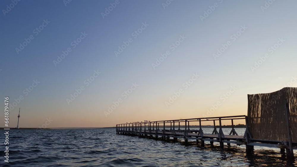 A lengthy wooden pier extends far from the shore, jutting into the calm waters of a peaceful body.