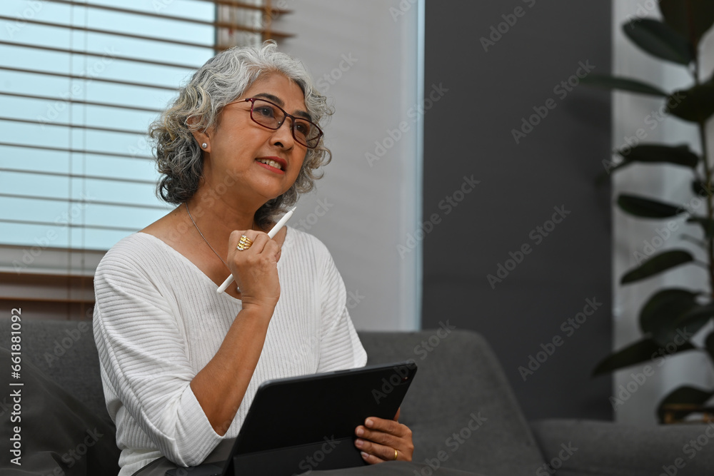 Portrait image of an Old Asian woman using a digital tablet while sitting on the sofa Portrait image of an Old Asian woman using a digital tablet while sitting on the sofa