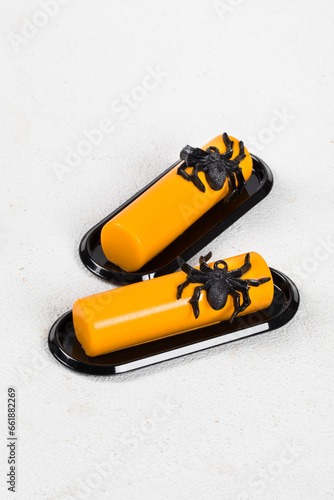 Pumpkin cream dessert bar, decorated with spider jelly on a black serving plate. White background. Halloween Holiday