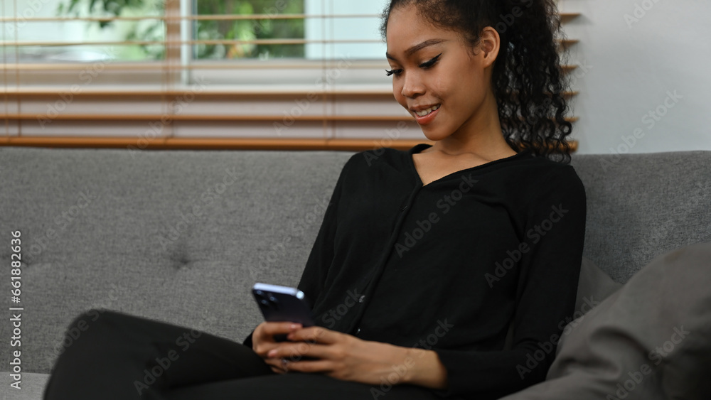 Cropped image of Smiling and Beautiful African teenage woman sitting on a couch at home and using a smartphone Cropped image of Smiling and Beautiful African teenage woman sitting on a couch at home and using a smartphone