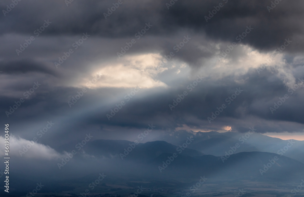 Naklejka premium sun beams over town in mountains during storm