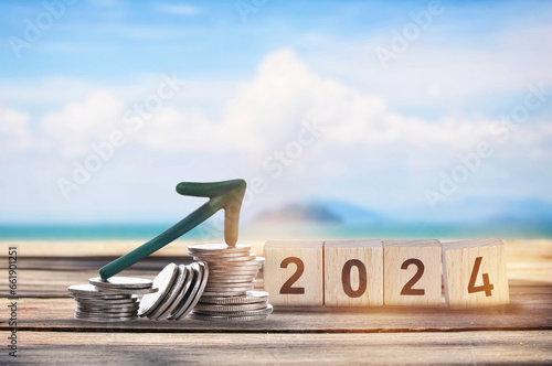 New year 2024 on wooden cube and stack of coins with arrow upwards on planks on tropical beach background. Business beginning with success and return on investment idea photo