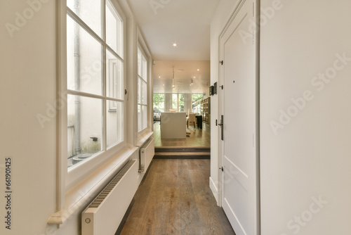 a long narrow hallway with white walls and wood flooring the room is well lit by the light coming through the window