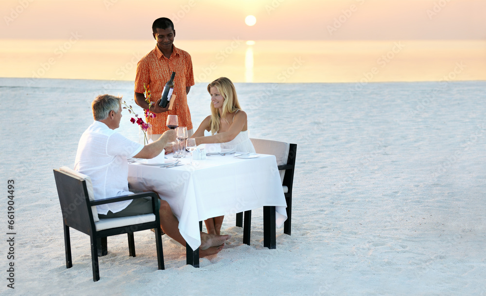 Couple, beach and dinner in sunset with waiter for romantic outdoor date, valentines day or anniversary. Man and woman with wine, cheers or celebration on table in relax or romance by ocean coast
