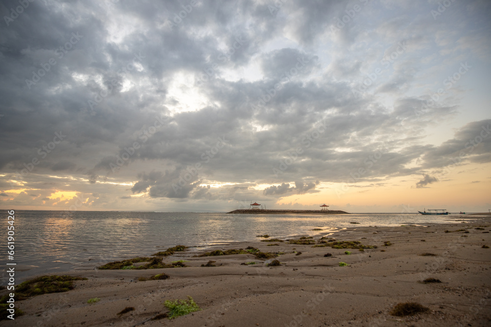 Beautiful sunrise on Sanur beach. Temple in the calm sea. Small waves in the morning. Sandy beach on the dream island of Bali. Sunset in a landscape shot, looking into the horizon