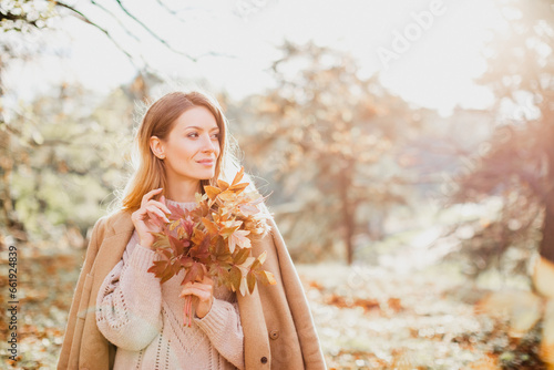 Happy young woman enjoying golden autumn on a warm sunny day. Beautiful portrait of a Caucasian girl in an autumn coat walks on a warm sunny day in the autumn park.