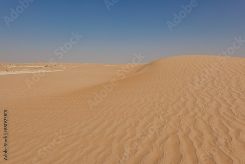 Red sand side dune with undulating vertical sand movements against the backdrop of a blue sky.