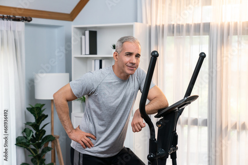 Active senior man running on elliptical running machine at home portrait as fitness healthy lifestyle and body care after retirement for pensioner. Clout