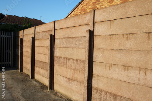 Concrete fence, made of concrete posts with stacked gravel boards blue sky background UK