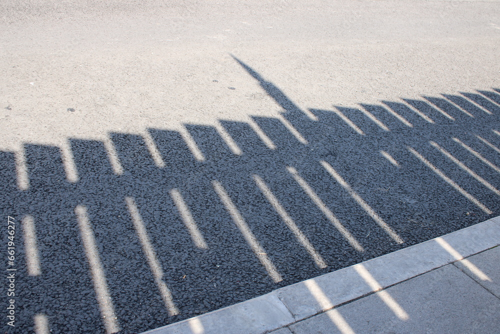 Fototapeta premium Detailed shadow of wooden fence on pavement and asphalt road