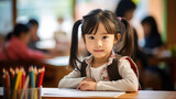 Little preschooler sits at a desk in the background of a classroom