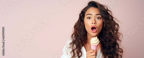 Surprised young woman with bright lips holding a delicious ice cream on flat pastel pink background with copy space. 