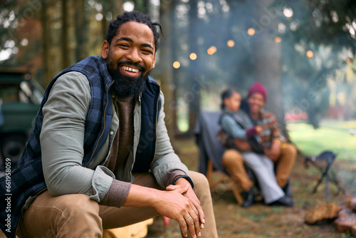 Happy black man camping with his family in forest and looking at camera. © Drazen