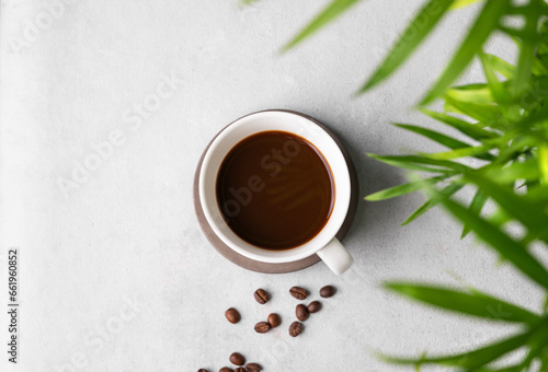 A cup of black aromatic coffee on a light background with coffee beans and a palm leaf. Morning energy drink concept.