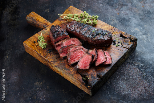 Barbecue dry aged angus roast beef steak with herb butter and dried oregano served as close-up on a rustic cutting board with copy space photo