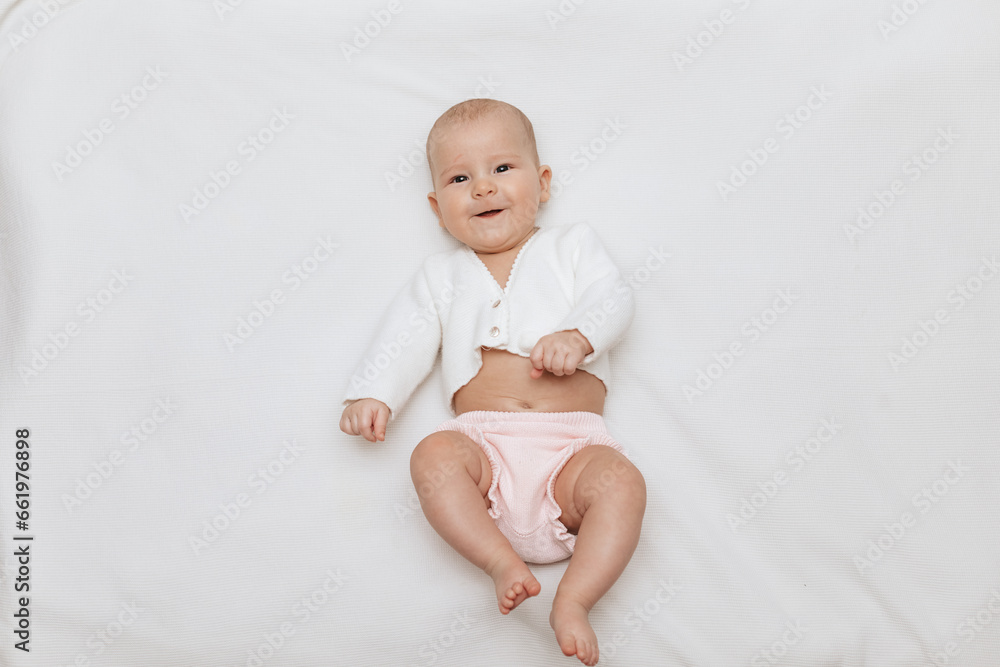 Funny newborn baby in a white knitted blouse and pink knitted underpants is lying on a white blanket. Copy space. Funny newborn baby in a white knitted blouse and pink knitted underpants is lying on a white blanket. Copy space.