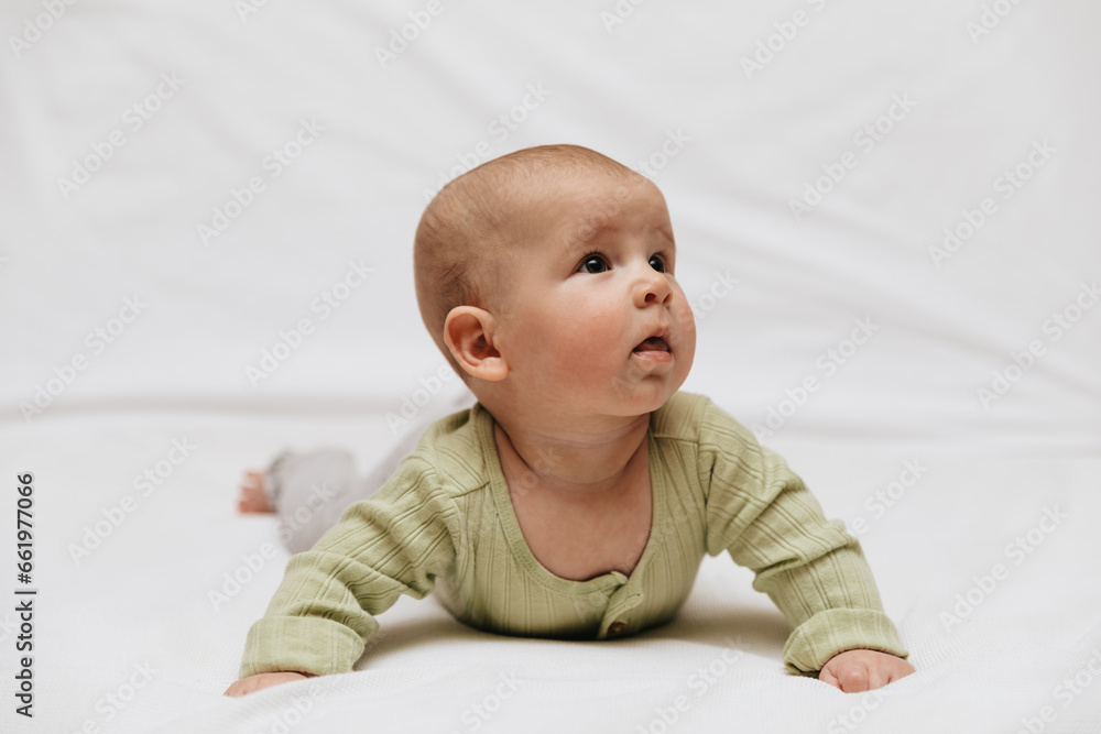 A girl in a green bodysuit and gray leggings is lying on stomach on a white background and looking to the side. Copy space. Close up. A girl in a green bodysuit and gray leggings is lying on stomach on a white background and looking to the side. Copy space. Close up.
