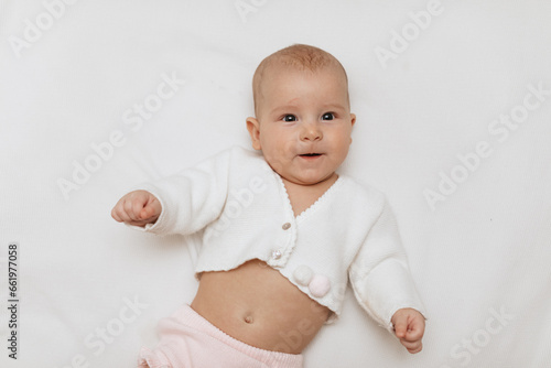Funny newborn baby in a white knitted blouse and pink knitted underpants is lying on a white blanket. Copy space. 
