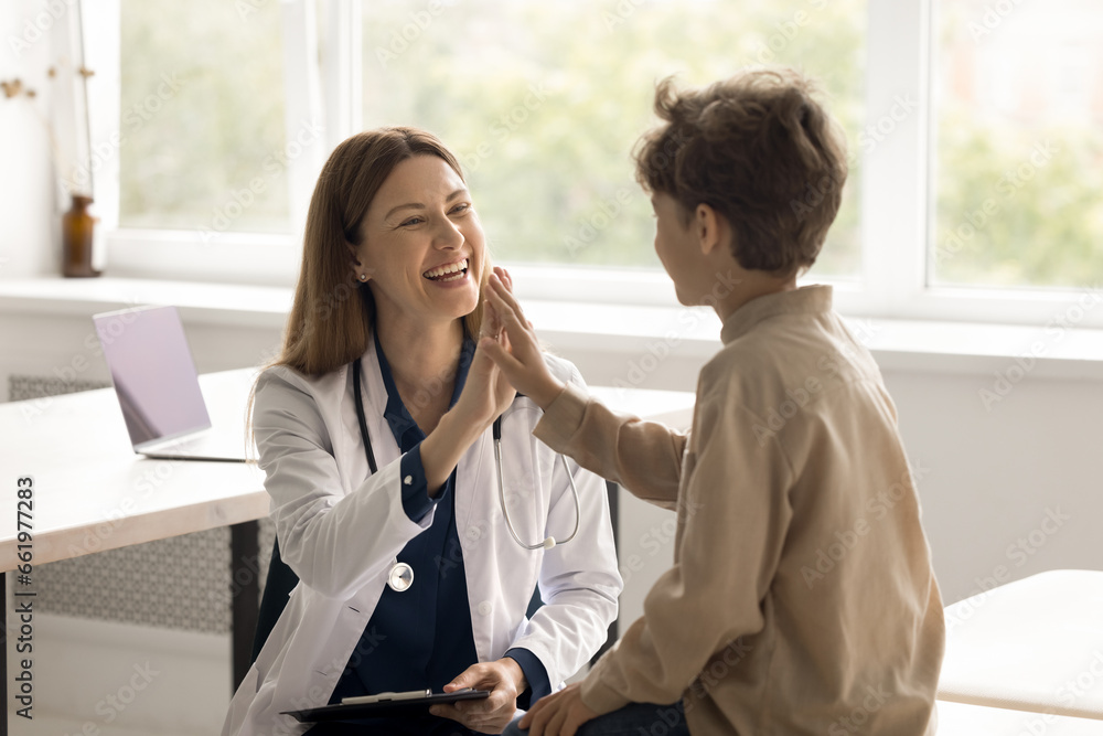 Happy little child boy patient giving high five to woman pediatrician in white uniform at consultation, celebrate successful treatment, finish meeting with friendly doctor. Good medical clinic service - obrazy, fototapety, plakaty 