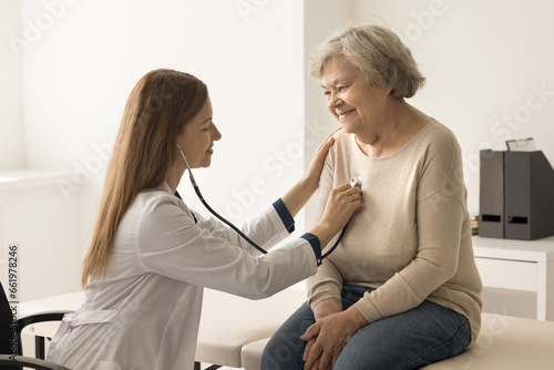 Cardiologist in coat examines older woman in clinic, listen to heartbeat with stethoscope during patient visit. Elderly woman passes heart check-up in hospital. Citizen healthcare services, cardiology photo