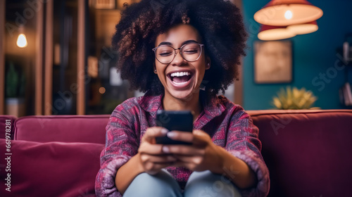 Excited happy young black woman holding smart phone device sitting on sofa at home photo