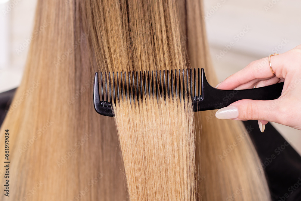 Fototapeta premium Hairdresser's hand brushing long natural blonde hair in beauty salon 