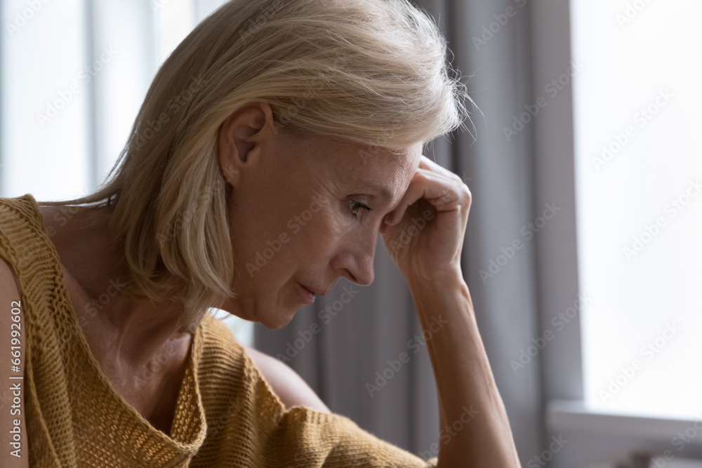 Sad thoughtful lonely elderly lady suffering from apathy, depression, mental disease, looking into vacancy, thinking over health problems, bad news, loss, grief, touching head. Side view Sad thoughtful lonely elderly lady suffering from apathy, depression, mental disease, looking into vacancy, thinking over health problems, bad news, loss, grief, touching head. Side view