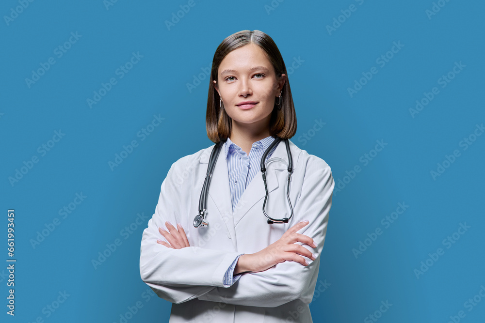 Portrait of young woman doctor student intern in white coat on blue background Portrait of young woman doctor student intern in white coat on blue background
