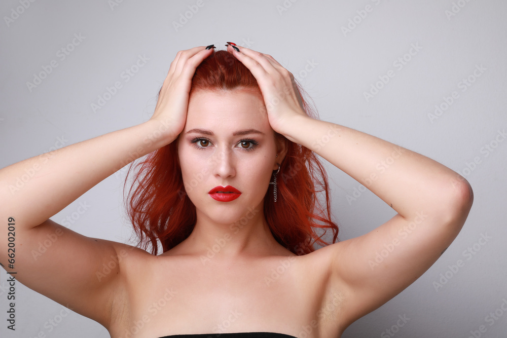 Indoor portrait of stunning young woman with long red hair over white wall. Indoor portrait of stunning young woman with long red hair over white wall.