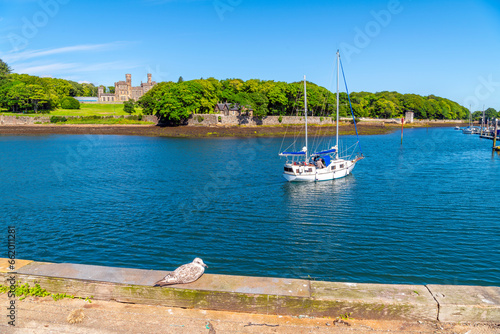 The imposing hilltop Lews Castle can be seen from the harbor port of the village of Stornoway, Scotland, as a seagull watches a boat sail on the sea. photo